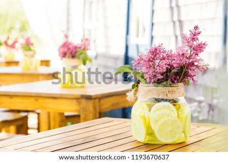 Bouquet of lilac flowers in a jar on the table. Jar filled with water with lemon slices. Photo in bright colors.