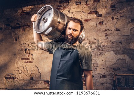Brewer in apron holds barrel with craft beer at brewery factory.