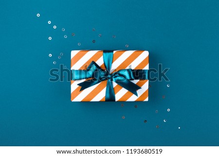 Gift box wrapped in red striped paper and tied with aqua blue bow on aqua blue background decorated with sparkles. Christmas card concept.