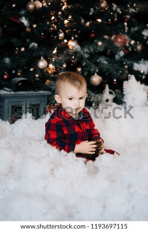 Beautiful little boy on the background of Christmas decor sitting in the snow. Happy Christmas and new year concept