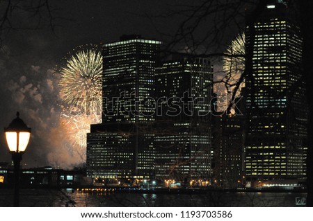 Fireworks explode behind Manhattan skyscrapers at night, New York East River in foreground.