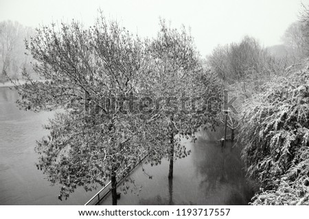 Winter Marne river flood. Embankment and park under high water in windy day with snowstorm. Paris suburb, France. Black and white photo.