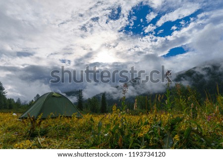 Tourist tent in a mountain valley on the background of clouds. Beautiful scenery.
