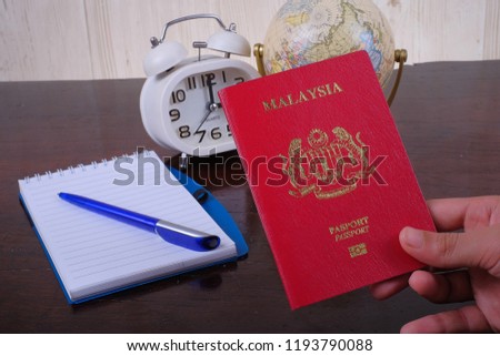 Accessories of travel concept with note book, globe, clock , money and alarm . Hand holding  passport on wooden background