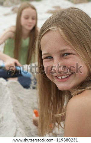 Portrait of a preadolescent girl smiling with sister playing in the background