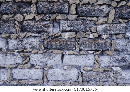 Stone wall, small stones forming square bricks. Ancient wall with broken and rusty stones.