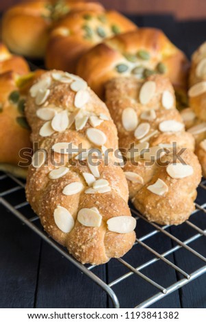 vertical picture of homemade fresh almond twist breads on oven grill on black wooden table.
