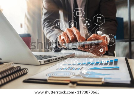 businessman or Designer using tablet with laptop and document on desk in modern office with virtual interface graphic icons network diagram.