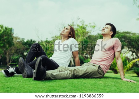 Portrait of two content handsome young men sunbathing, relaxing and sitting on grass in park. Relaxation in park concept.