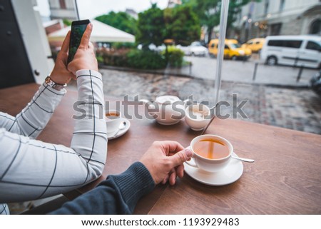 couple sitting in cafe drinking warm up tea in cold autumn day. woman taking picture on phone for instagram. first person view