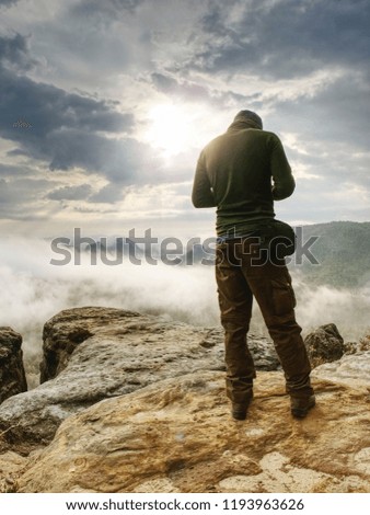 Photographer bend head check display of camera. Man stay on cliff and takes photos. Autumn beautiful misty landscape misty sunrise at horizon