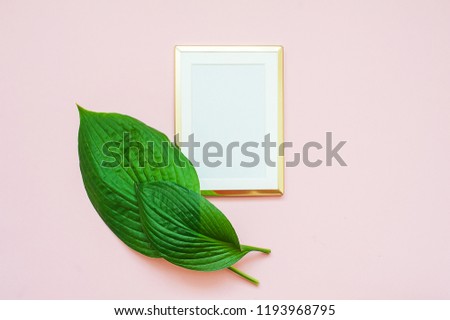 Gold photo frame with tropical leaves on pink background. Mock up frame with copyspace. Flat lay, top view.