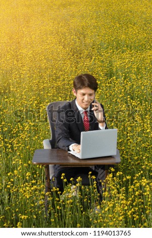asian businessman  talking on smartphone and looking at laptop outdoor