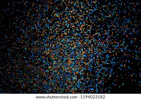 Thousands of confetti fired on air during a festival at night. Image ideal for backgrounds. Blue and yellow are the prevaining color in the picture. The sky as background is black.