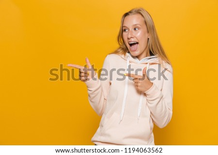 Photo of adorable school girl with dental braces pointing finger aside at copyspace isolated over yellow background