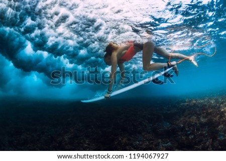 Professional surfer woman with surfboard make duck dive underwater with ocean wave.