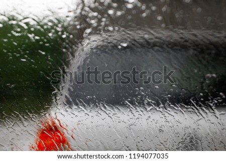 Driving carefully in bad weather bokeh backgrounds. Raindrops on car windshield selective focus on droplets the other car in front with breaks lights turned on - Car driving and weather concept.