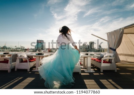The bride spins back and dances in a stylish dress, looking away, with rooftop restaurant, terrace overlooking the city.
