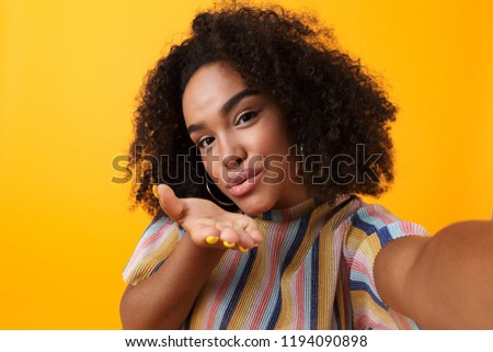 Image of beautiful young happy african cute girl posing isolated over yellow background take a selfie blowing kisses.