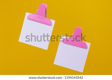 White paper notes with paper clip holders isolated on yellow background.