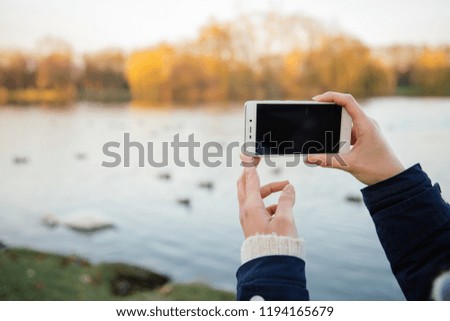 A young girl takes pictures by phone. Autumn. Park background 