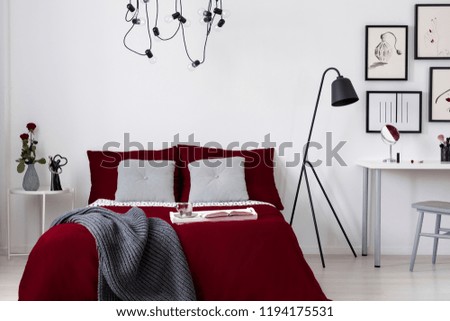 A burgundy bedding and gray pillows on a bed in a white wall bedroom interior. Real photo.