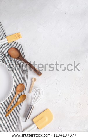 Kitchen utensils for baking concept - White ceramic tart pan, Whisk, wooden spoons, silicone spatula, basting brush on Crumpled Striped Napkin. Top view, Flat lay, Copy space.
