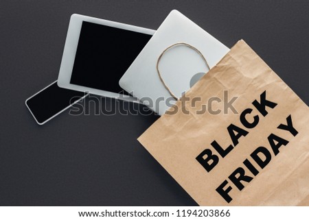 top view of digital devices in shopping bag with black friday symbol on black