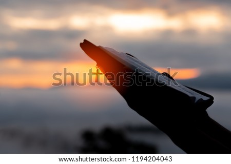 Silhouette of human hand holding bible and cross, the background is the sunrise., Concept for Christian, Christianity, Catholic religion, divine, heavenly, celestial or god. Royalty-Free Stock Photo #1194204043