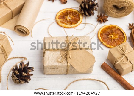 Gifts from craft paper, dried orange, cinnamon, pine cones, anise on a white table. The original decor for Christmas.