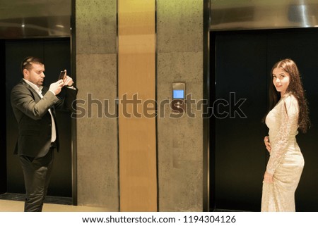 man in suit photographs on smartphone beautiful girl with long hair in the lobby of hotel