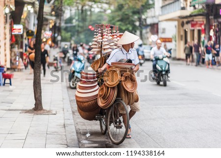 Hanoi, Vietnam - October 15, 2016. Street vendor with a bicycle on the streets of Hanoi, Vietnam. Selling traditional hats in the middle of busy traffic in the capital city. Royalty-Free Stock Photo #1194338164