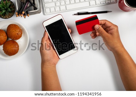 Online payment Concept. Man using credit card with mobile phone and coffee cup on white office desk.