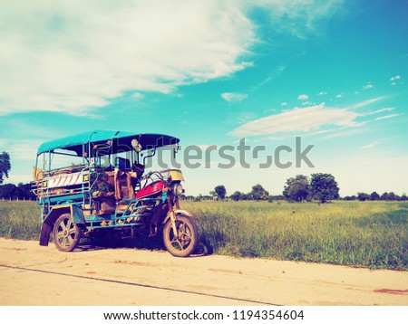 Old tricycle of farmer park on the road near green paddy field front of tree and blue sky background beautiful landscape field of Thailand harvest with sunlight.