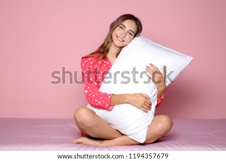 Beautiful teen girl hugging pillow on bed against color background