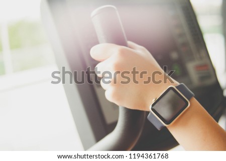 A woman’s hands holding on the handle of the cardio machine and wearing a sport smart watch in a gym.