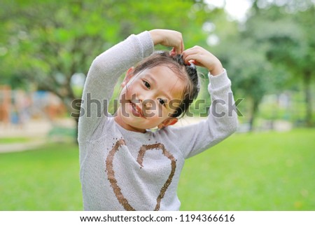 Portrait of smiling cute little Asian child girl in green garden with making her hands for heart sign.