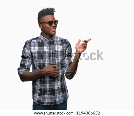 Young african american man wearing sunglasses over isolated background with a big smile on face, pointing with hand and finger to the side looking at the camera.