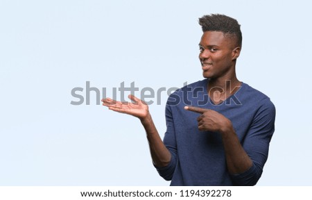Young african american man over isolated background amazed and smiling to the camera while presenting with hand and pointing with finger.