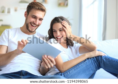 Young couple watching media content online in a tablet sitting on a sofa in the living room. Royalty-Free Stock Photo #1194398065