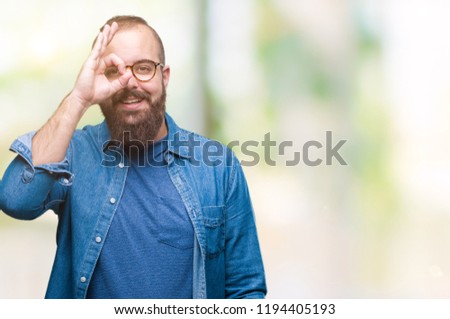 Young caucasian hipster man wearing glasses over isolated background doing ok gesture with hand smiling, eye looking through fingers with happy face.