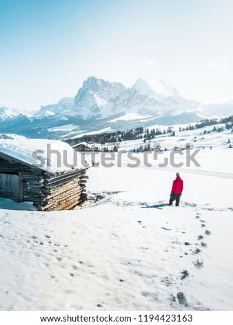 Hiker in red jacket enjoy classic view of the famous Alpe di Siusi mountain resort or Seiser Alm in the Dolomites in winter, South Tyrol, Italy. Mountain rocky peak above valley.