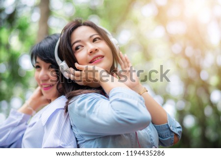 Young carefree attractive Asian women enjoy to listening music in garden, friendship concept.