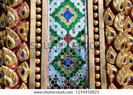 Close up of wall is decorated with stained glass small plate. Traditional Thai golden mosaic art on the wall of temple.