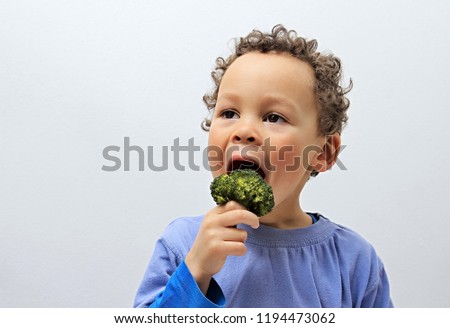 little boy eating broccoli with grey background stock photo