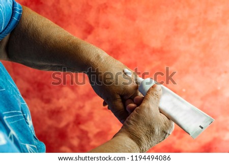 Hands of an elderly woman moisturizing skin cream. Care for old skin. Focus in the center. Red background. Royalty-Free Stock Photo #1194494086