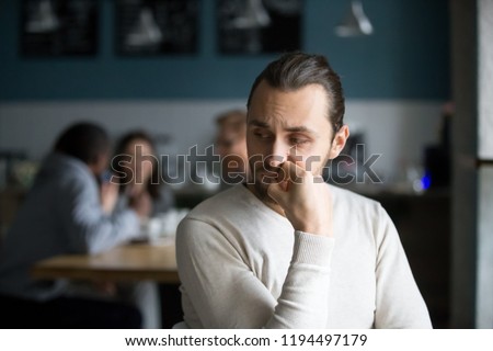 Upset millennial outsider feel offended lack company, young outcast guy suffer from discrimination, jealous of friends hang out together in café, envious male loner depressed sit alone in coffeeshop Royalty-Free Stock Photo #1194497179