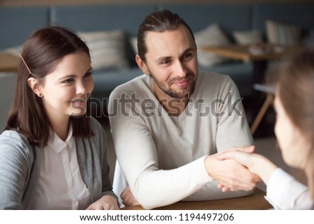 Excited young couple handshake broker buying home or renting apartment closing deal, happy millennial man and woman shake hand of realtor making agreement or signing contract of successful investment