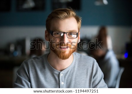 Portrait of smiling red haired millennial man looking at camera sitting in café or coffeeshop, happy young male in glasses posing for picture working at laptop or studying out in coffeehouse Royalty-Free Stock Photo #1194497251