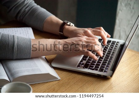 Close up of man typing at laptop studying out in café, busy guy working at computer at café table with books and coffee on it, serious male message on keyboard sitting in coffeeshop using gadget